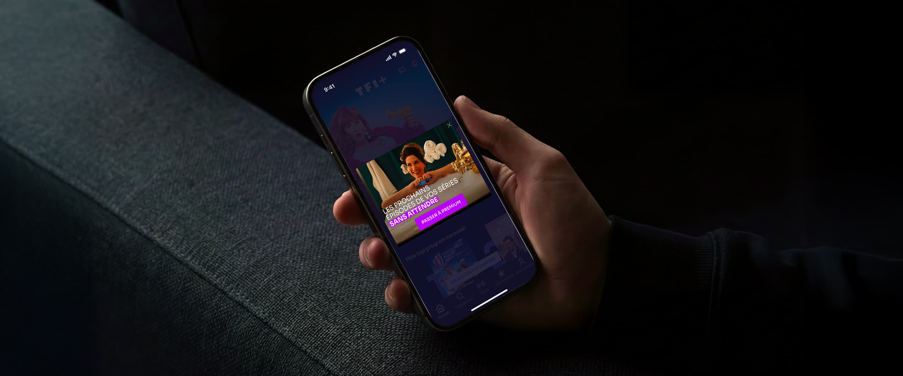 Main tenant un smartphone affichant l'interface TF1+ Premium, avec un bandeau violet 'Passer à Premium' mettant en avant les épisodes en avant-première sans publicité.